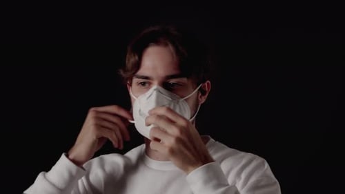 Trendy Young Man putting on and removing facemask, covid-19 protection, close, black background