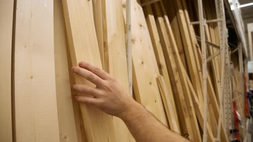 Customer Examines Pine Boards in Building Supply Lumber Aisle Hands Pull Planks From Stack Assessing