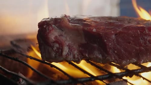A cook turns a grilled steak amid flames, smoke and barbecue coals. Close-up.