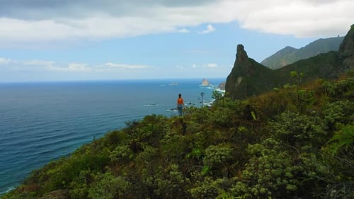 Aerial Woman Stands on Cliff Edge with Ocean Mountain View