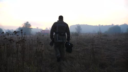 Firefighter Walking in Field Towards Fire Truck at Sunset