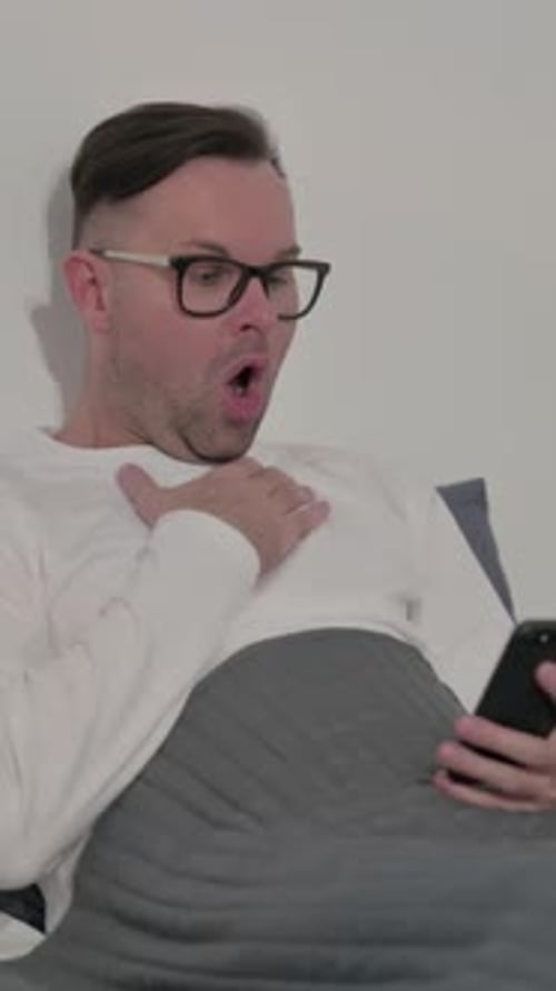 Casual Man Reacting to Loss on Smartphone in Bed, Vertical Video
