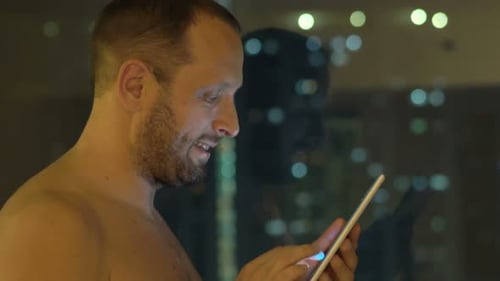 Shirtless Man Using Tablet at Night by Window