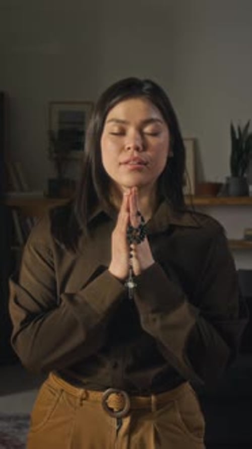 Young Woman Praying with Rosary Beads in Home