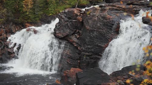 A tranquil waterfall cascades over dark rocks, its gentle flow harmonizing with the serene ambiance