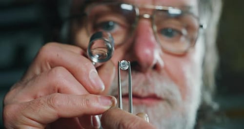 Slow motion macro close up of experienced goldsmith controlling a quality of diamond stone, select