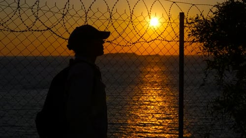 Woman Silhouette Looking at Sunset Behind Barbed Wire Fence