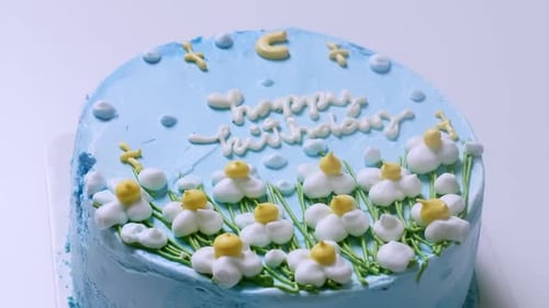 Zooming out of a close-up shot of a blue frosted birthday cake, decorated with small white flowers w