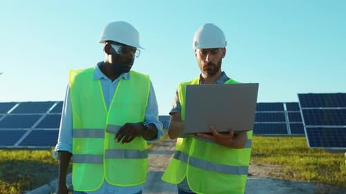 Slow Motion African American and Caucasian Engineers Walking with Laptop on the Solar Farm in
