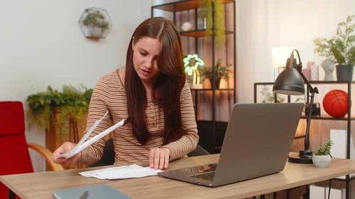 Junge Frau gibt Kreditkartennummer auf dem Laptop ein, bezahlt Rechnungen, Schecks und drückt zur Bestätigung auf „Bezahlen“