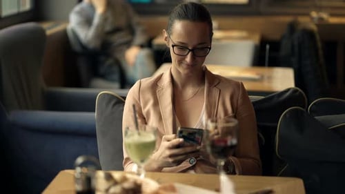 Woman Texting On Smartphone And Drinking Beverage In Cafe