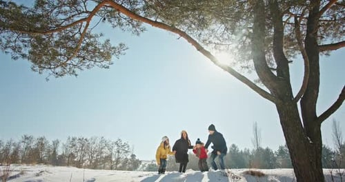 Family Has Fun Jumping on Hill with Snow Near High Pine Tree
