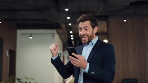 Man Celebrates Success While Reading Phone in Office