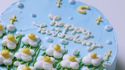 A close-up shot of a birthday cake with blue creamy frosting and decorated with white and yellow flo