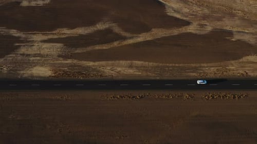 Car driving on a road, close to desert dunes, sunset in Namibia - Aerial tilt reveal