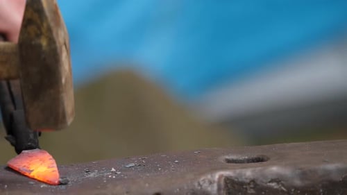 Blacksmith shaping knife from hot steel on anvil with hammer. Close up