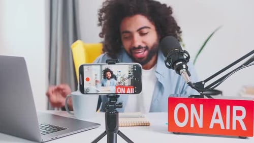 Young Inspired Arabian Man Blogger Records Video on Phone Sits at Table
