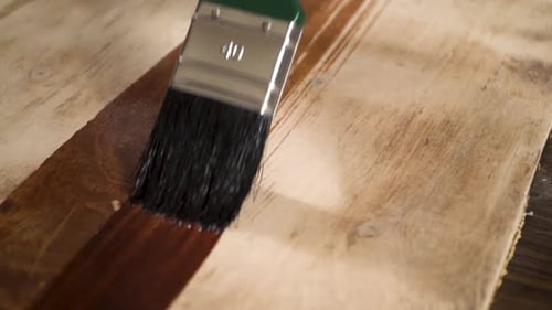 Close shot of a paint brush putting wood oil on a wood