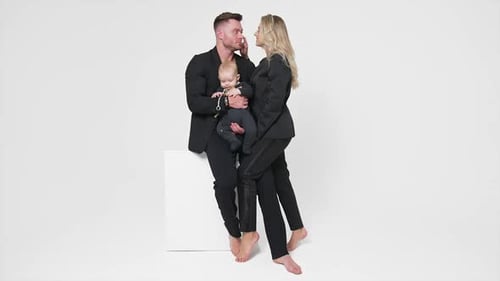 Loving couple in black suits with their little child. Family portrait of young family in studio.