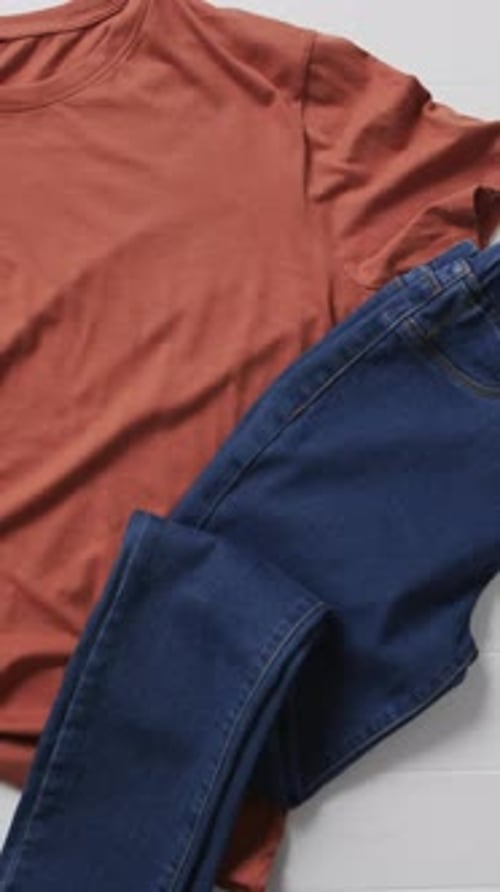 Vertical video of orange t shirt, denim trousers, shoes and copy space on white background