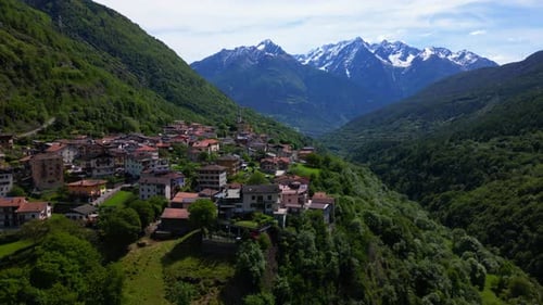 Alpine village of Malonno nestled in mountain valley with snow peaks and summer greenery visible