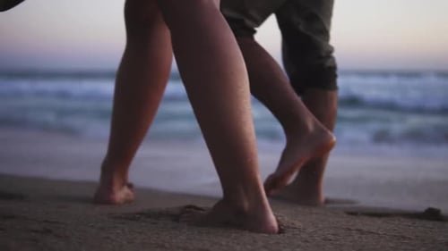 Slow motion low angle handheld shot of a couple in love walking at dusk on a beautiful sandy beach i