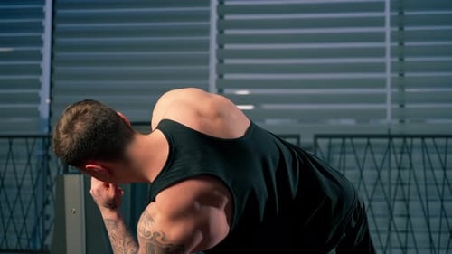 Nahaufnahme im Fitnessstudio Junger gutaussehender Kerl mit Tattoos in einem schwarzen T-Shirt pumpt seine seitlichen Bauchmuskeln auf dem