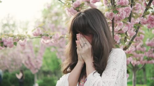 Young Woman Cries Near Blossoming Pink Trees