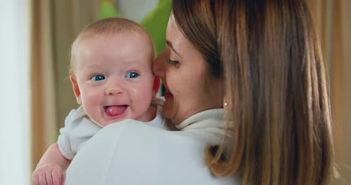Close-up. Happy woman kisses a newborn baby. Young mother holding her little son. Beautiful Happy Fa