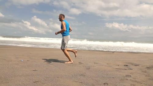 Young man jogging on sandy beach near sea in super slow motion