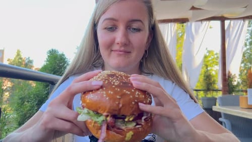 Blonde Woman Eating a Double Hamburger in a Fast Food Restaurant A Hungry Woman Who Eats Deliciously