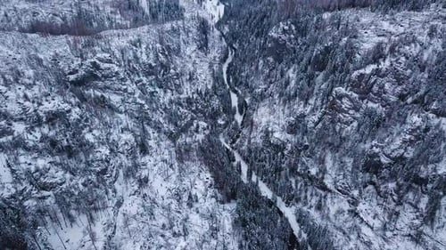 Tilt-Down Drone Shot of a Dark River in a Snowy Mountain Landscape