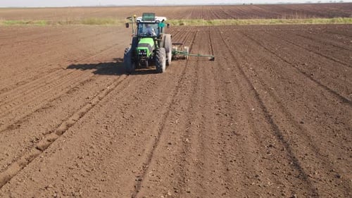 Aerial drone shot of a farmer in tractor seeding, sowing agricultural crops at field.