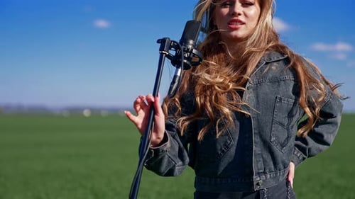 Girl singing in green field. Beautiful woman singing with microphone in green field