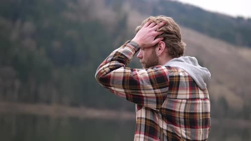a thoughtful looking man swings his gaze to the left while running his hand through his blond wavy h