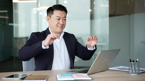 Happy asian businessman finished work on laptop sitting at desk at workplace in business office.