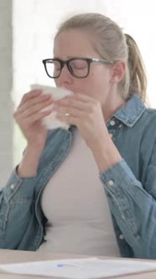 Woman Sits at Desk Blowing Her Nose with Tissue