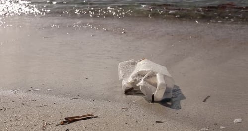 Discarded plastic bottle on sandy beach with gentle waves in the background, environmental issue