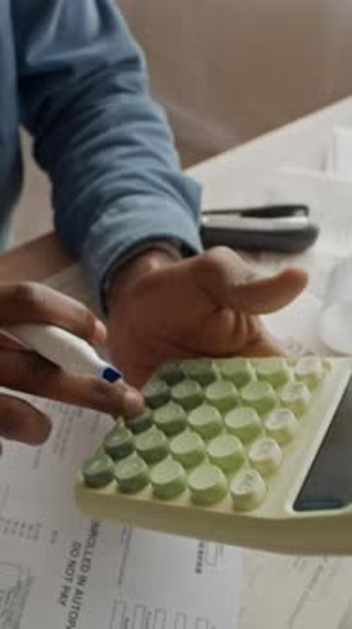 Vertical of Black Man Using Calculator to Organize Finances at Messy Table