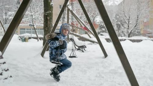 Slow motion of boy swinging in a playground during a winter snowfall