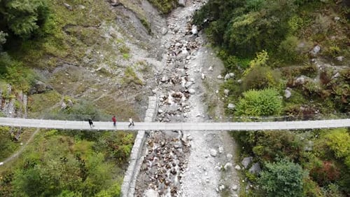 Tourists Crossing Over The Hanging Bridge At The Valley Within Annapurna Circuit In Nepal. aerial