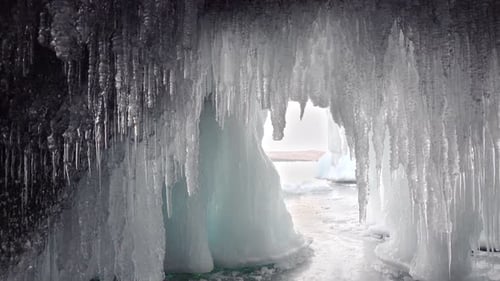 Foreground are many spiky translucent icicles. Looking out from the ice cave.