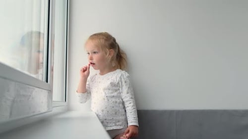 Cute Child Enjoys Lollipop near Window