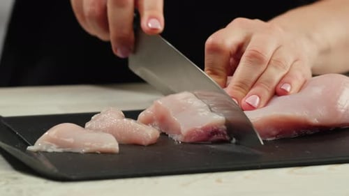 Homme tranchant un filet de dinde ou de poulet cru sur une planche à découper en chêne, cuisine en gros plan avec un couteau