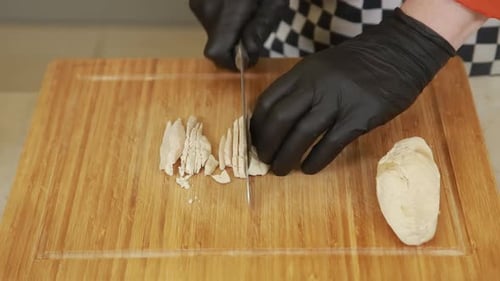 Chef cortando finamente o filé de frango cozido em cubos pequenos em uma tábua de corte de madeira
