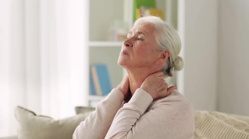 Senior woman massaging neck while sitting on couch