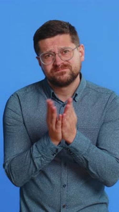 Man pleading with hands together against blue background