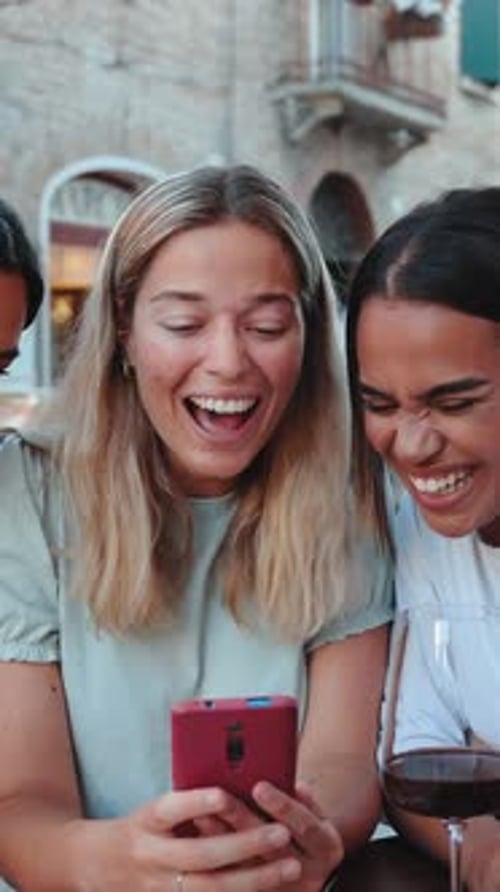 Three Young Adults Laughing at Smartphone at Cafe