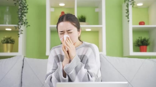 Young Woman Sneezing on Couch at Home