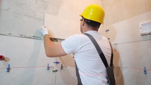 Construction Worker Applying Gray Tile to Wall